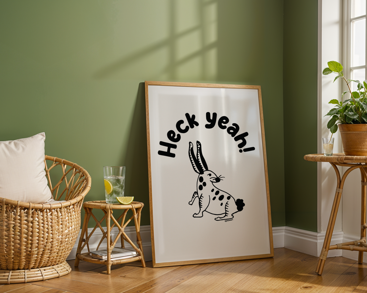 Living room with green walls showing a framed print on the floor with handwritten bubble letters spelling out “Heck Yeah!” Illustrated rabbit character in black on a white background with clean lines. Inspired by the southwest and western United States.