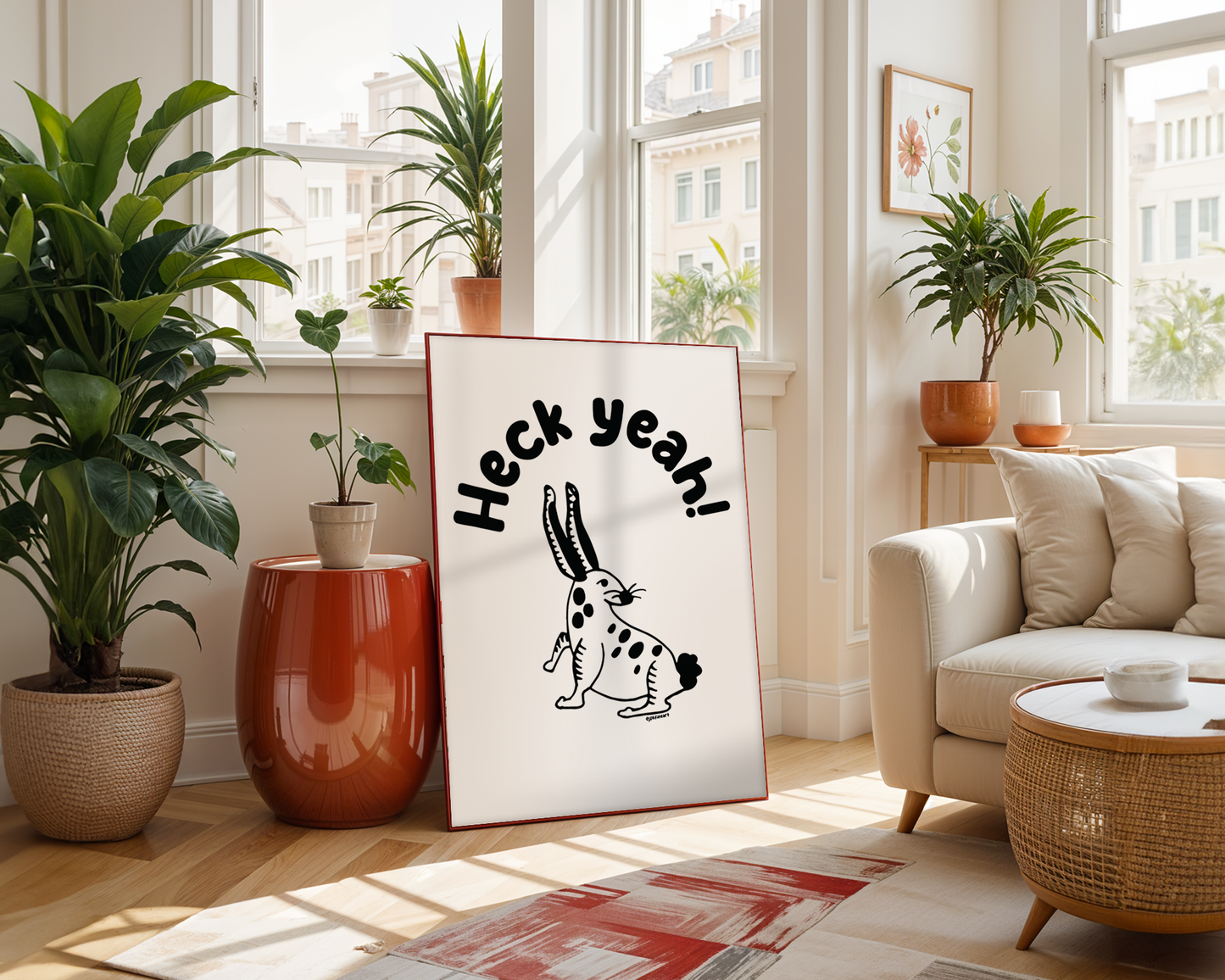 Living room with modern furniture showing a framed print on the floor with handwritten bubble letters spelling out “Heck Yeah!” Illustrated rabbit character in black on a white background with clean lines. Inspired by the southwest and western United States.