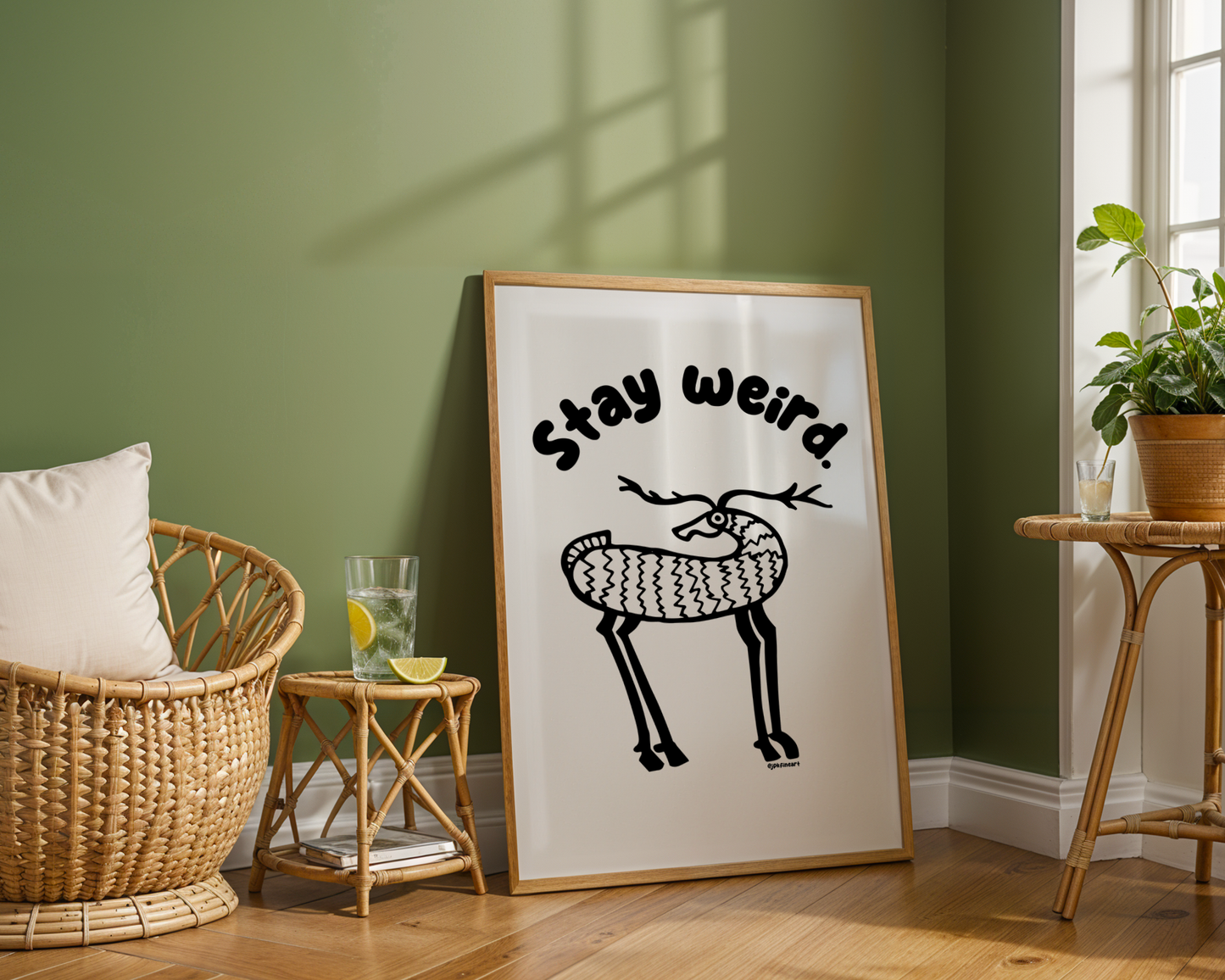A room with green walls shows an oversized frame with print showing handwritten bubble letters spelling out “Stay Weird” Illustrated deer character in black on a white background with clean lines. Inspired by the southwest and western United States.