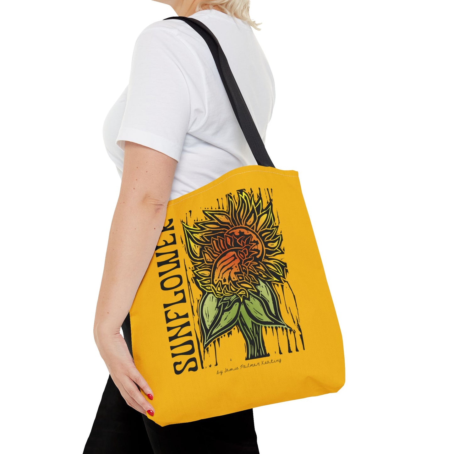 Person holding a yellow tote bag with sunflower design and text.