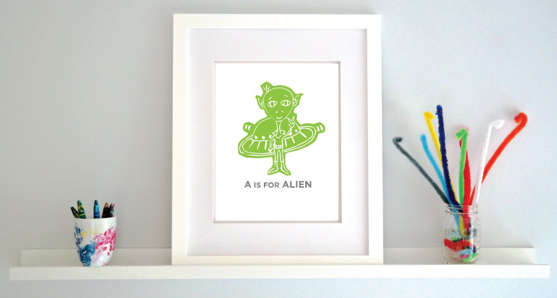 Friendly illustrated alien giving the peace sign in front of his UFO with "A is for Alien" text in a gray block font below.
