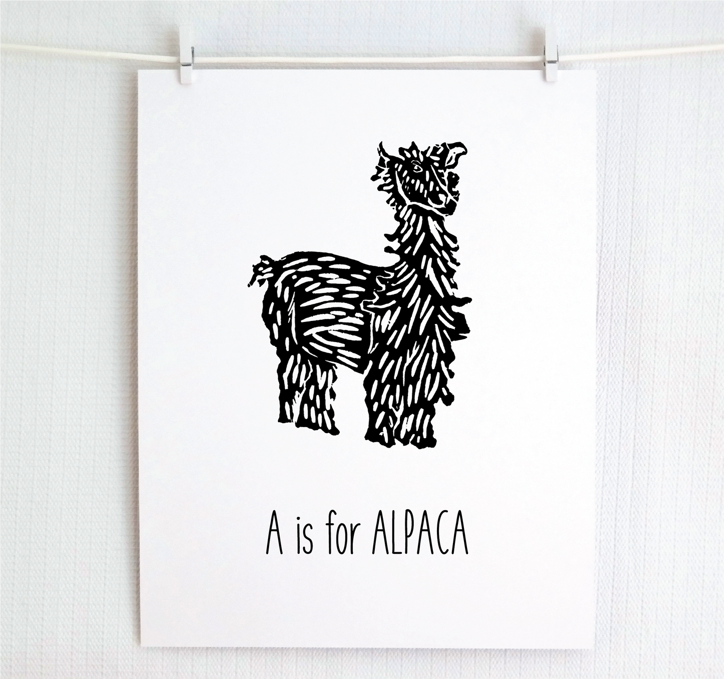 An illustrated alpaca with textured fur stands over hand written style block lettering text that says “A for Alpaca.”