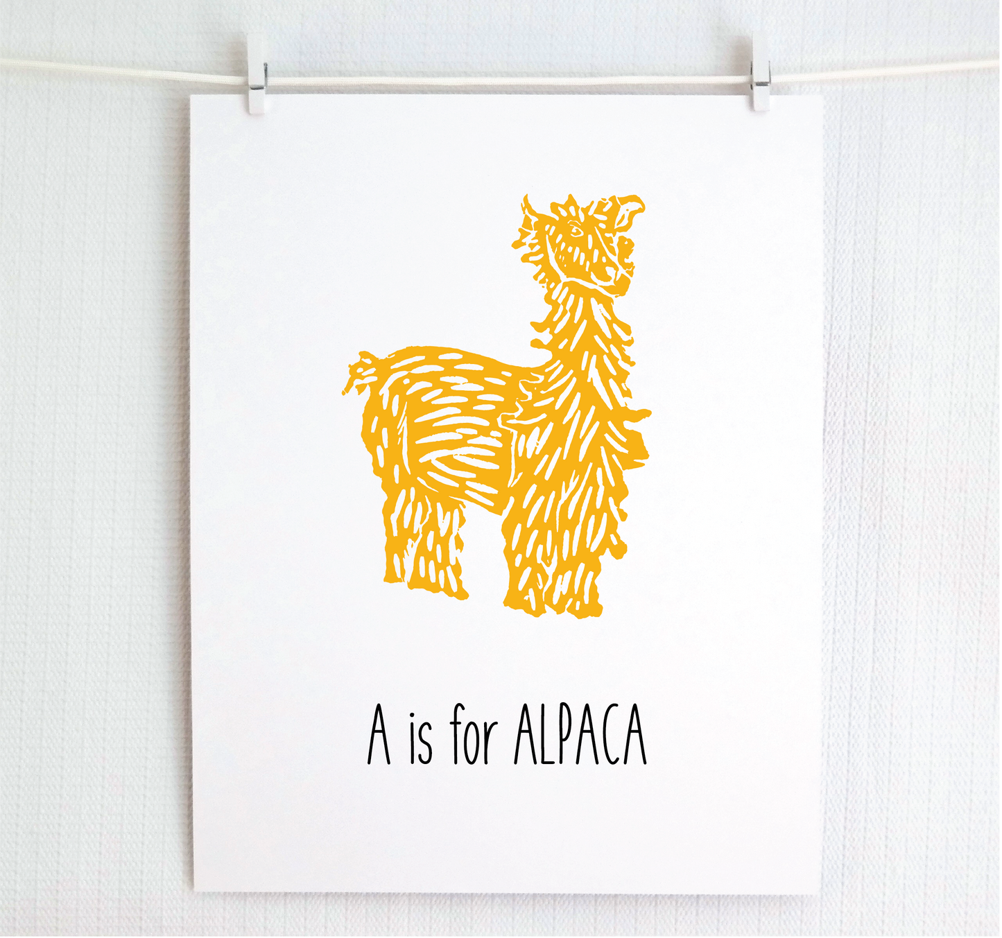 An illustrated alpaca with textured fur stands over hand written style block lettering text that says “A for Alpaca.”