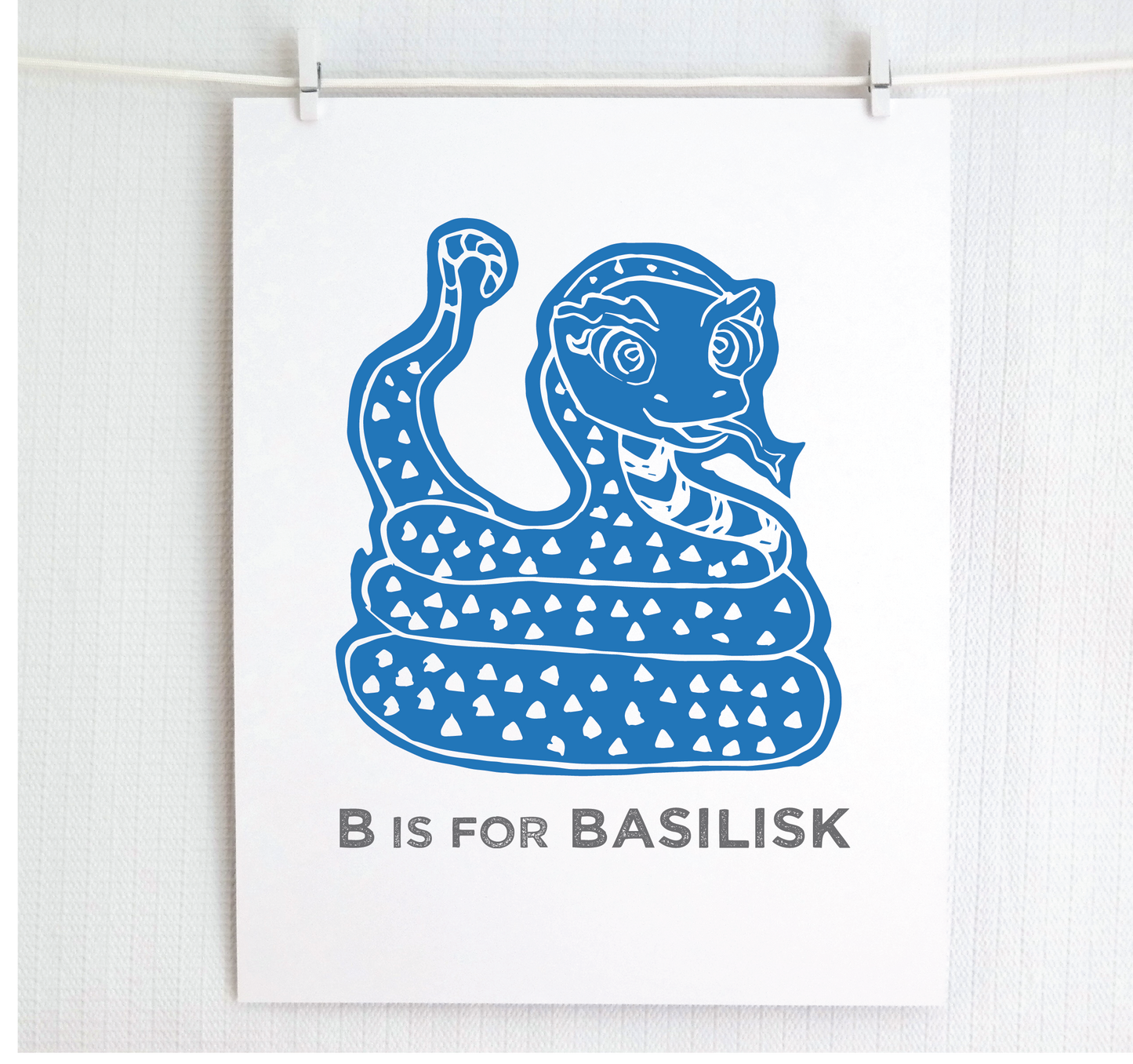Friendly illustrated basilisk giving a slithery smile above “B is for Basilisk” text in a gray block font below.