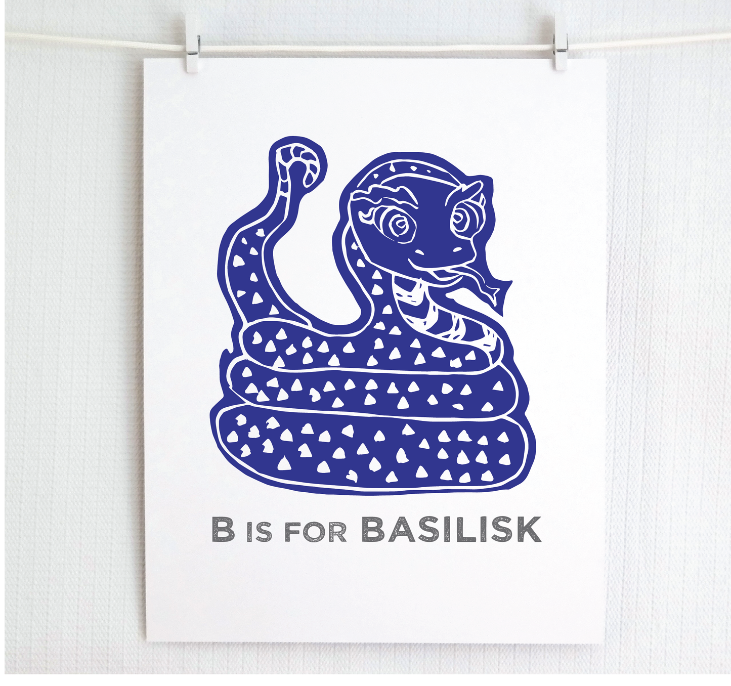 Friendly illustrated basilisk giving a slithery smile above “B is for Basilisk” text in a gray block font below.