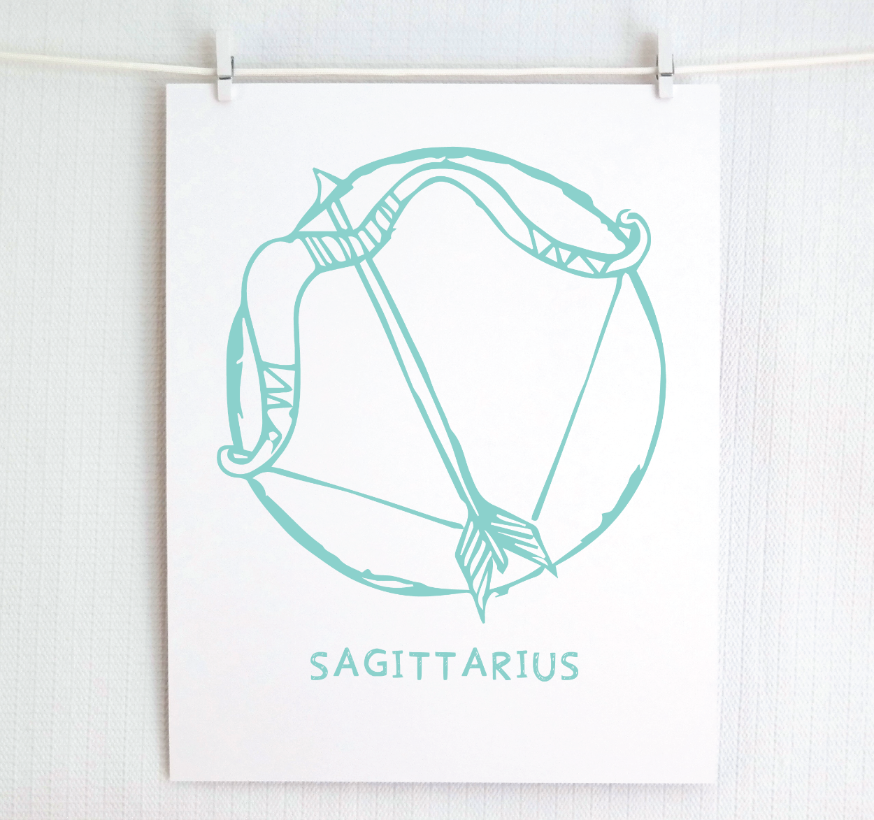 An illustration of the SAGITTARIUS Zodiac sign as a bow and arrow, printed on paper with the word ‘SAGITTARIUS’ at the bottom in teal.