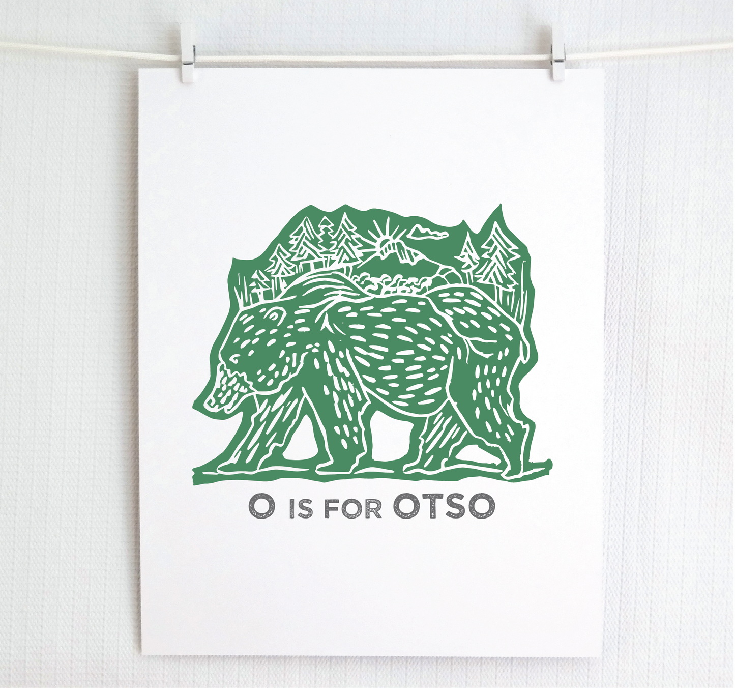 Friendly illustrated bear walking with the forest growing on his back. “O is for Otso” text in a gray block font below.