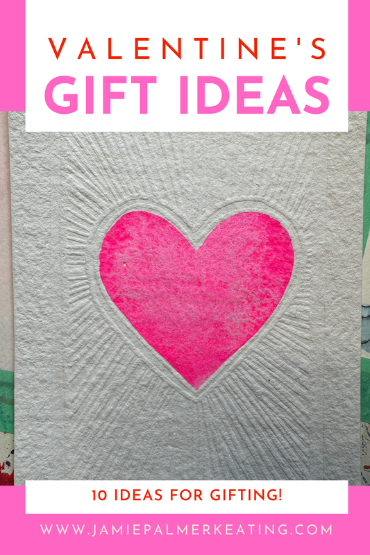 A vibrant pink watercolor heart sits in the center of embossed rays and textures on a natural fiber watercolor sheet of paper.