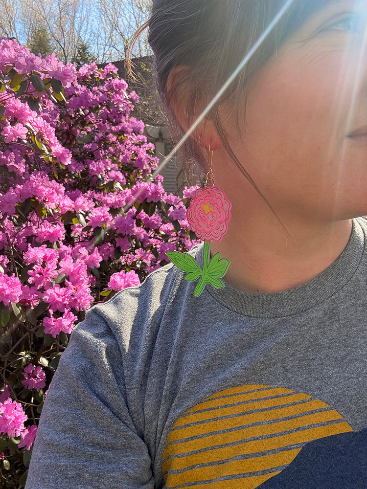 Flower earring on a woman in front of a pink flower bush