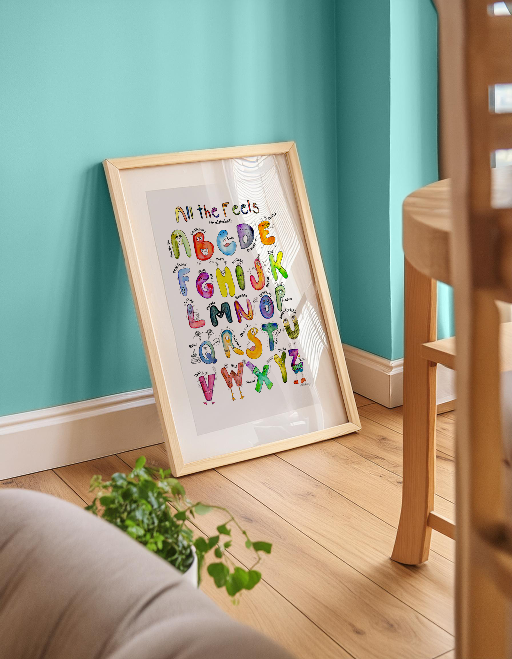 Framed alphabet poster on a teal wall with wooden furniture and a plant.