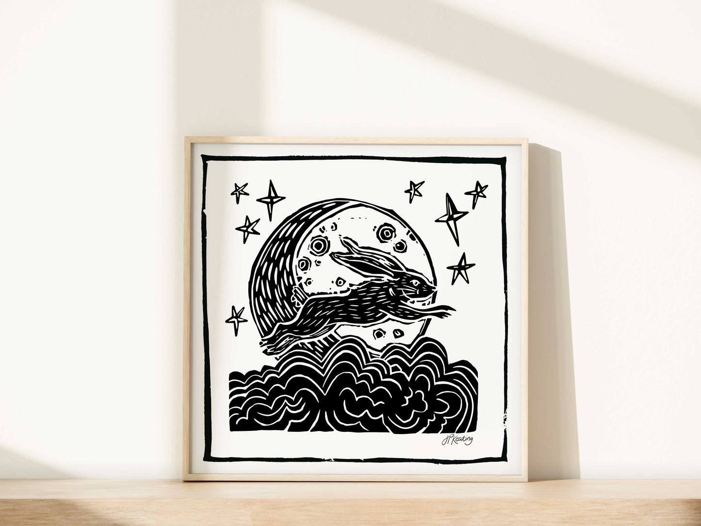 Framed black and white artwork of a stylized bunny jumping over a moon with stars on a white wall.