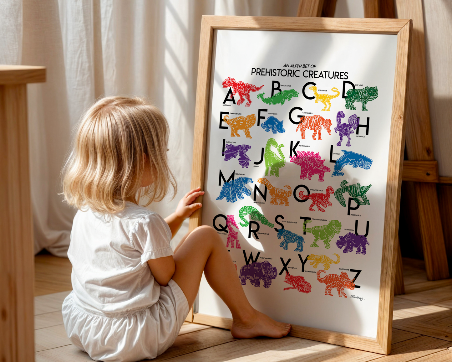 Small child sits in front of a colorful, illustrated prehistoric creatures for every letter of the alphabet printed on a white background. Modern, slim text in black. Color palette is red, lime green, dark green, light blue, red, orange, pink and purple.
