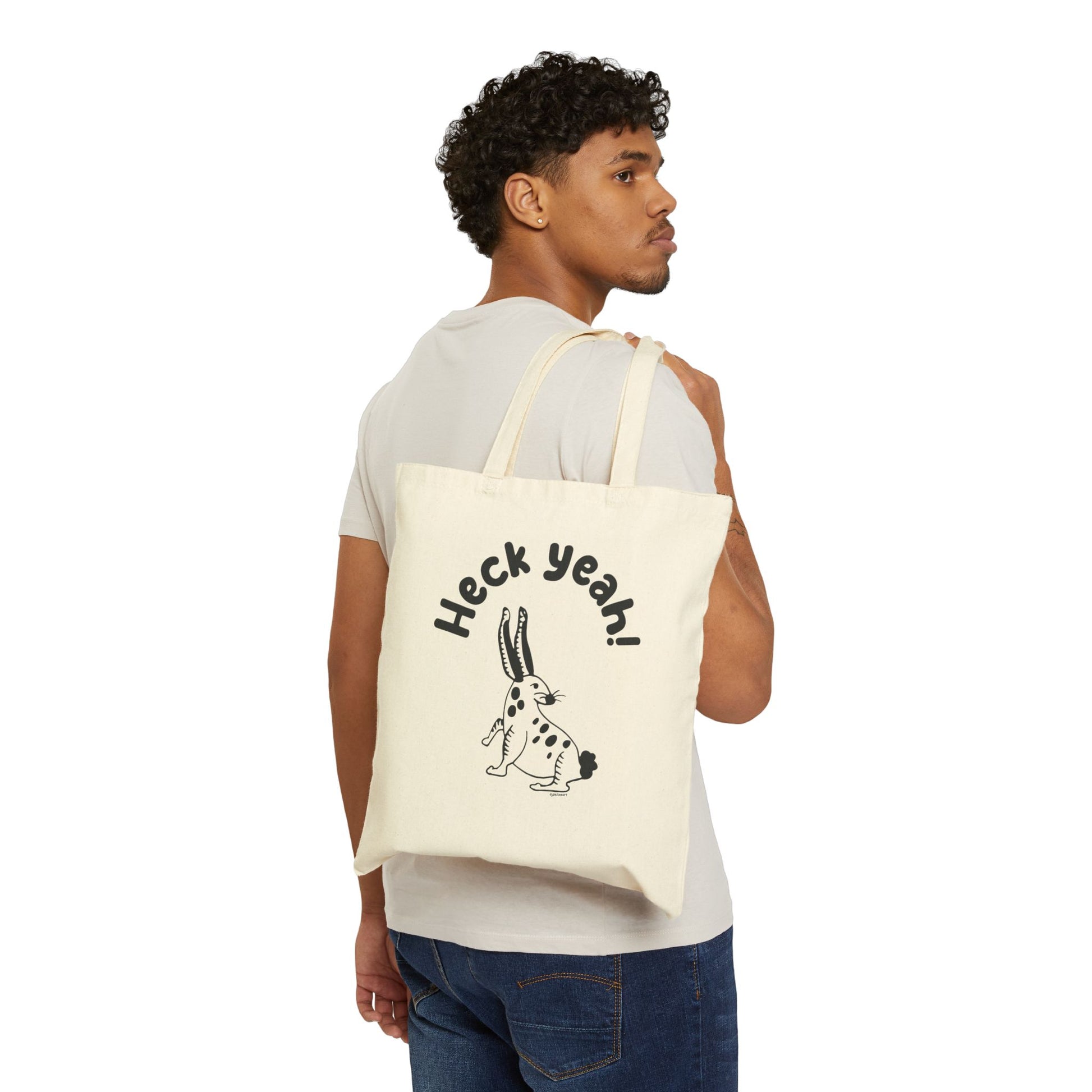 Man carrying a tote bag with a Heck Yeah with a rabbit graphic design on a white background