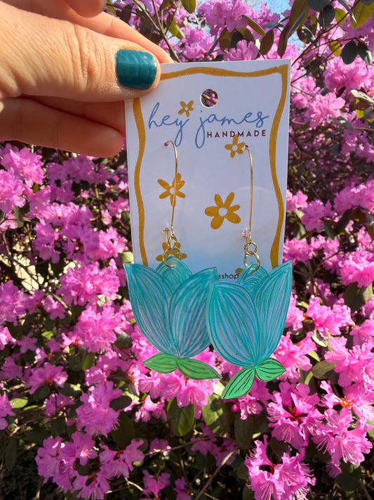 Turquoise earrings on a card held in front of pink flowers