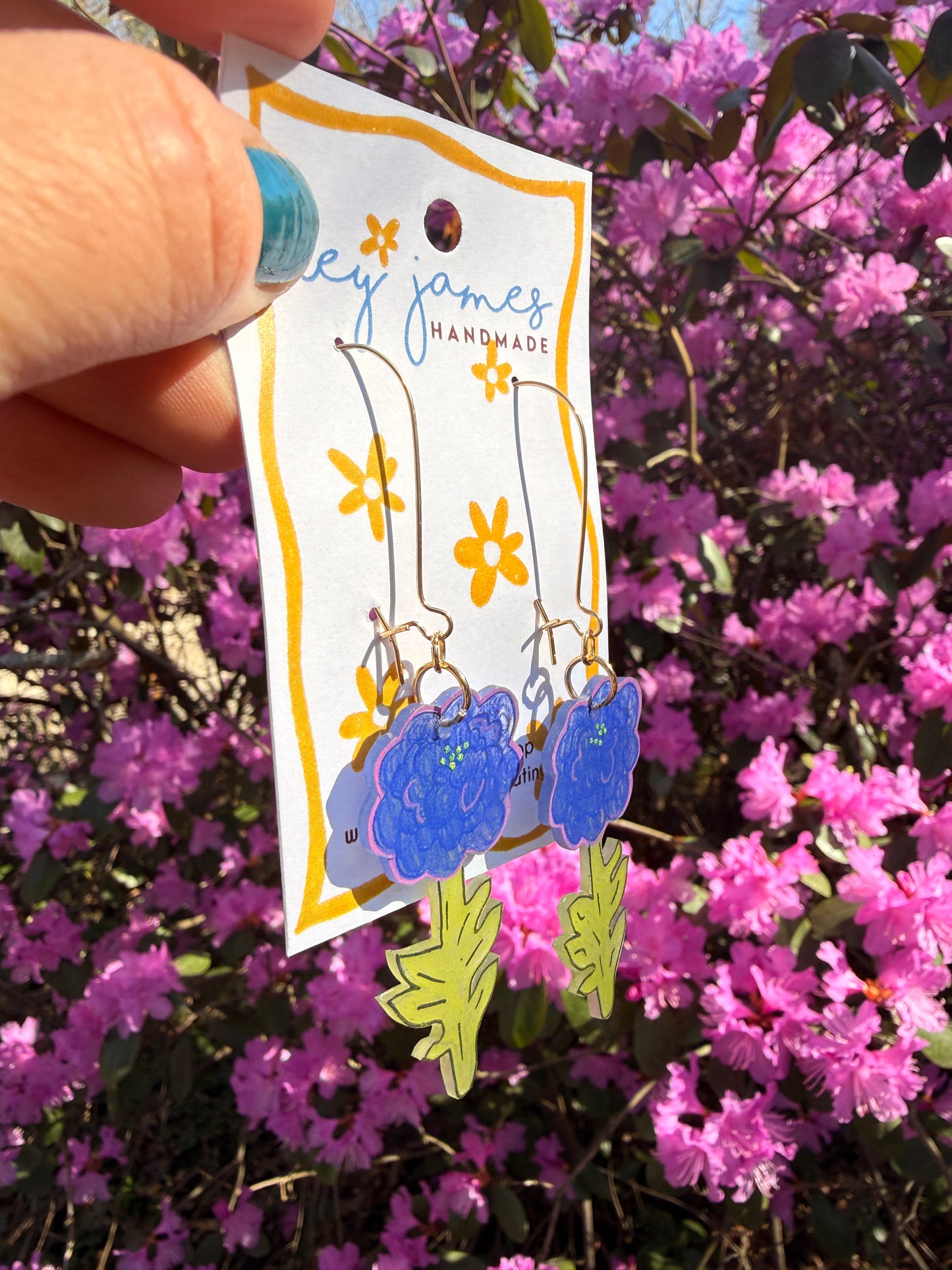Handmade earrings held in front of pink flowers