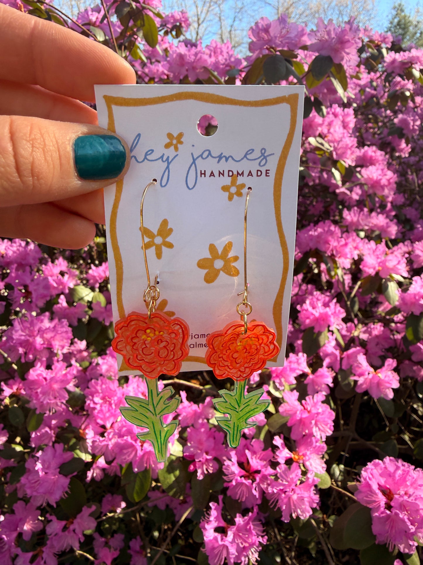 Hand holding a card with floral earrings against a background of pink flowers