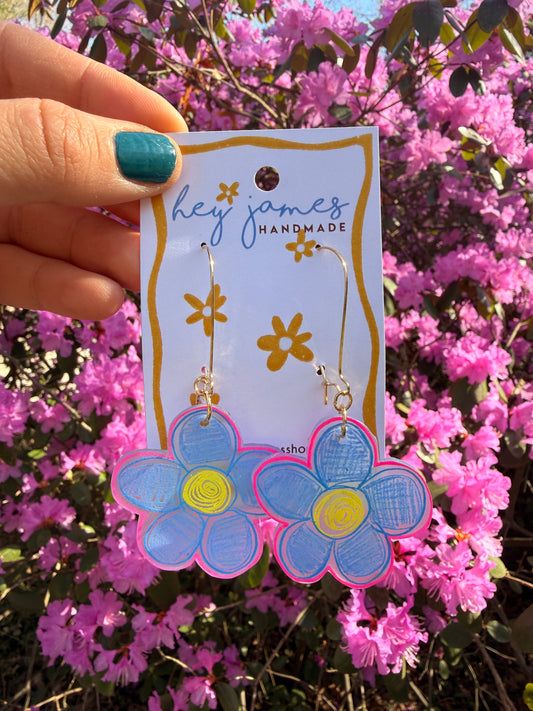 Flower-shaped earrings on a 'hey james' card held in front of pink flowers