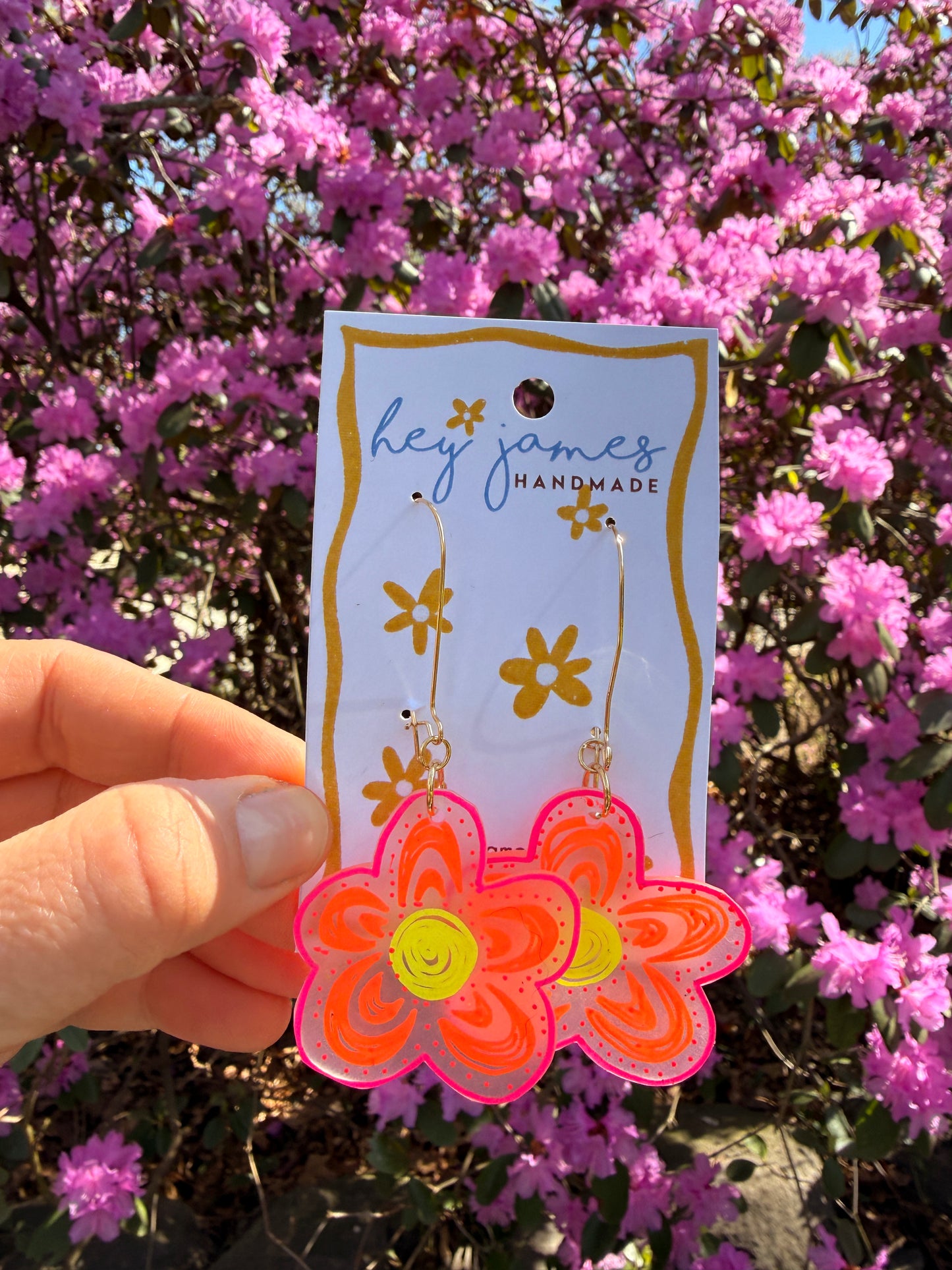 Hand holding a card with floral earrings against a background of pink flowers