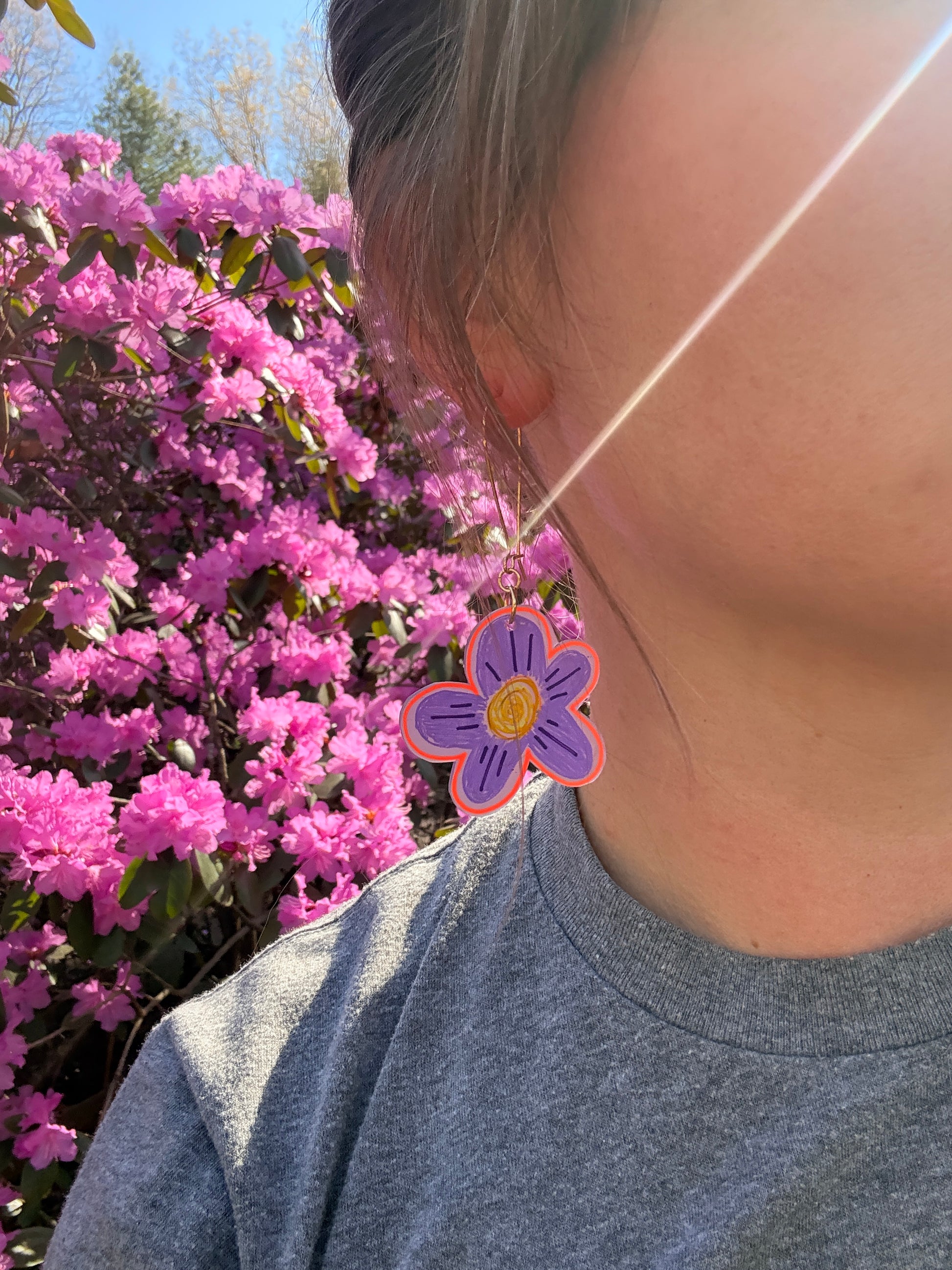 Person wearing a gray tank top with a purple flower design, standing next to pink flowers.