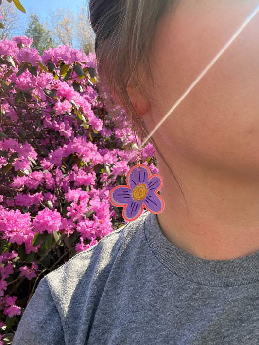 Person wearing a gray tank top with a purple flower design, standing next to pink flowers.