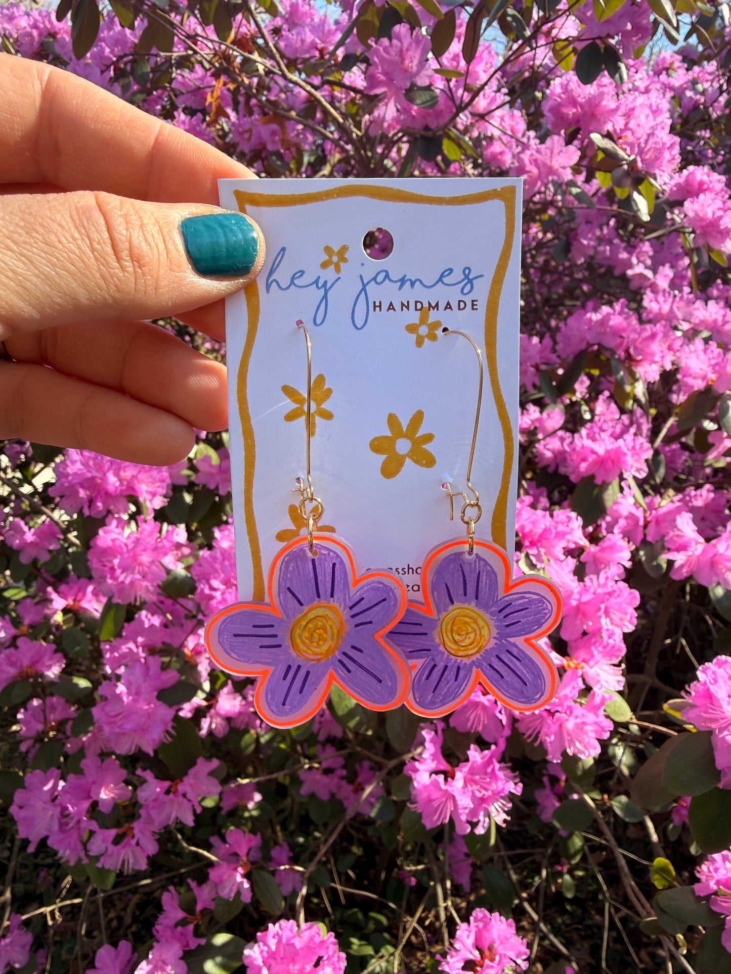Hand holding a card with floral designs against a background of pink flowers