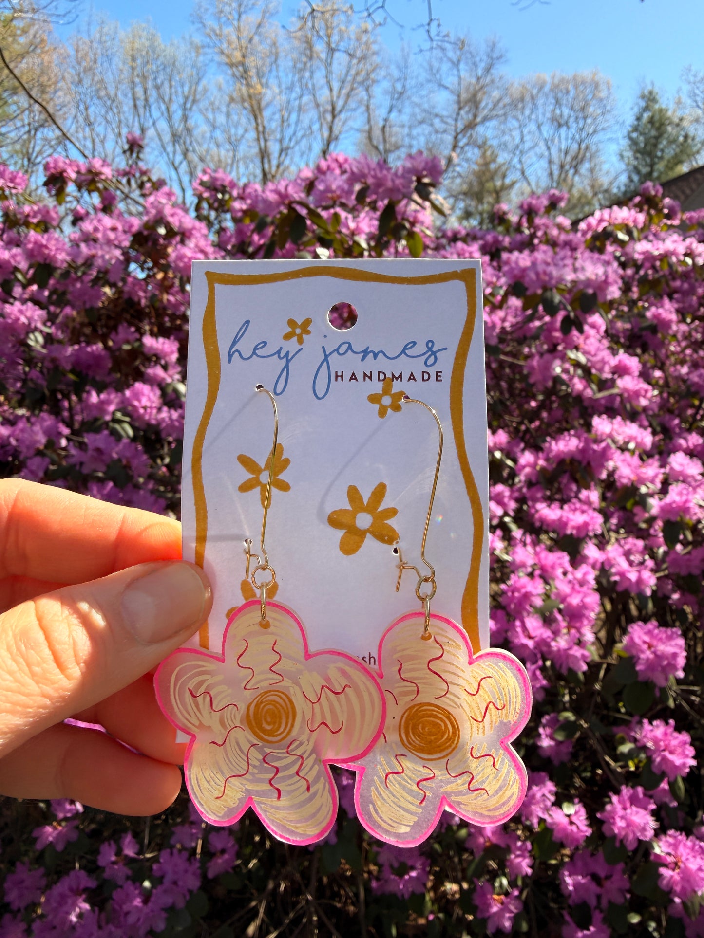 Handmade flower-shaped cardearrings with 'hey james handmade' branding held in front of pink flowers.