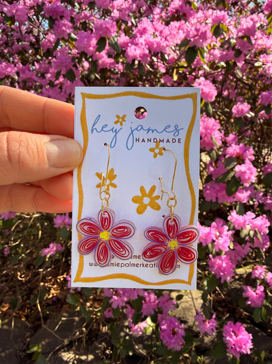 Handmade jewelry with floral designs held in front of pink flowers