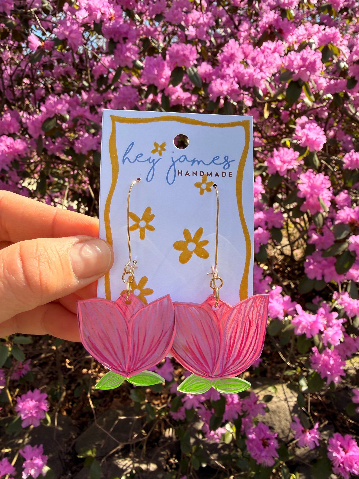 Pink flower-shaped earrings held in front of a floral background