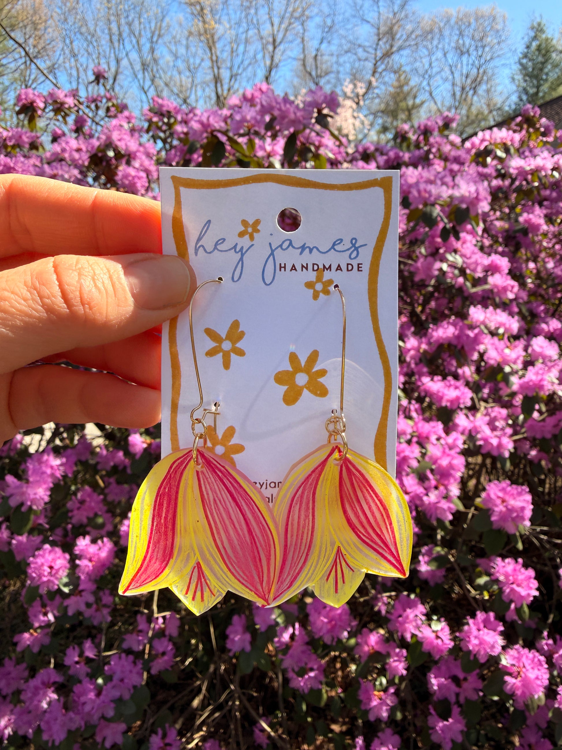 Flower-shaped earring on a card held in front of pink flowers