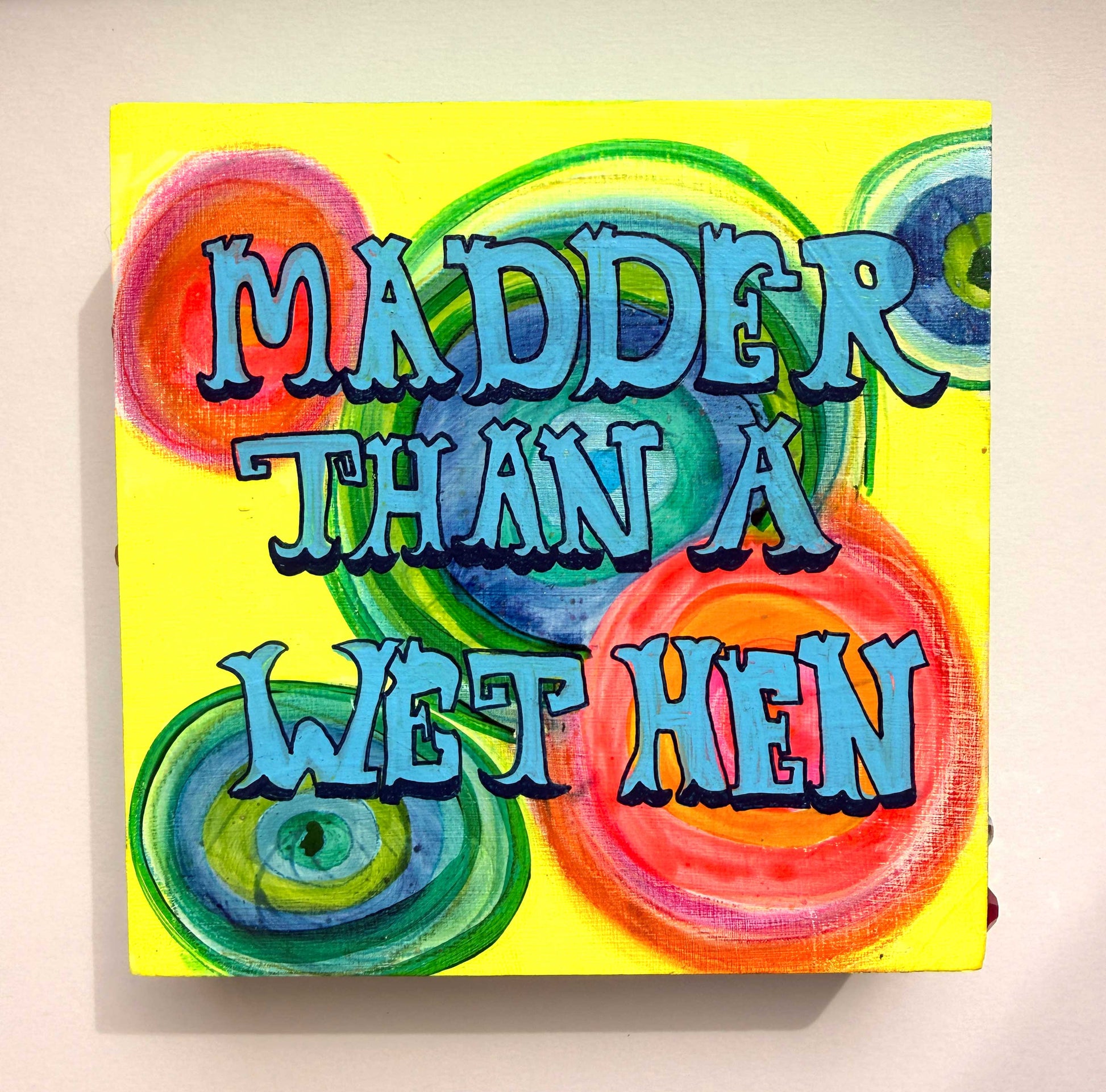 Colorful text artwork with 'Madder Than A Wet Hen' on a yellow background