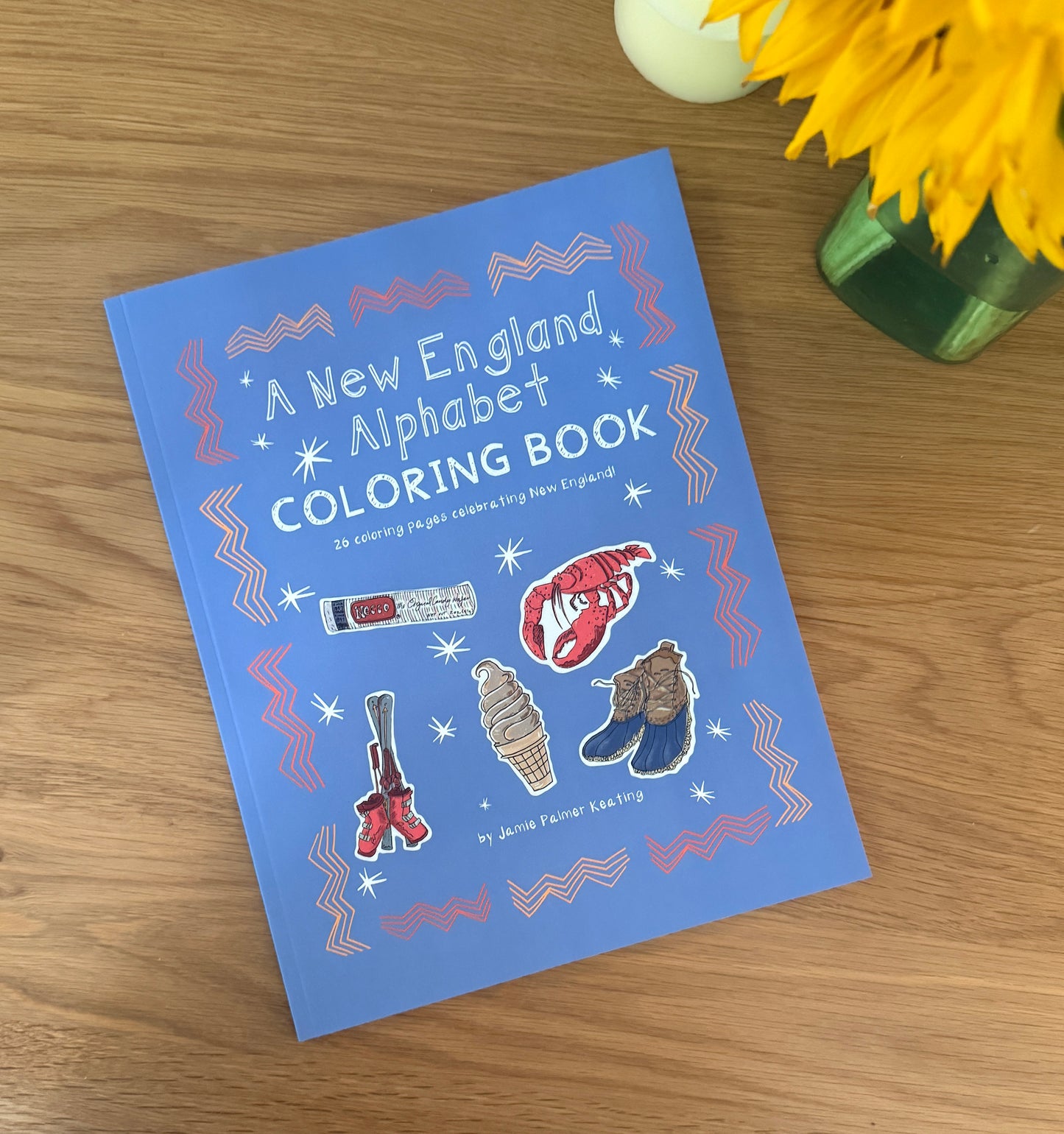 Coloring book titled 'A New England Alphabet' on a wooden surface with flowers in the background