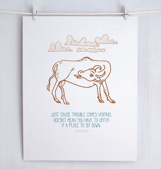 A digital archival print of an original illustration featuring a cow with mountains in the background, displayed on a white wall.