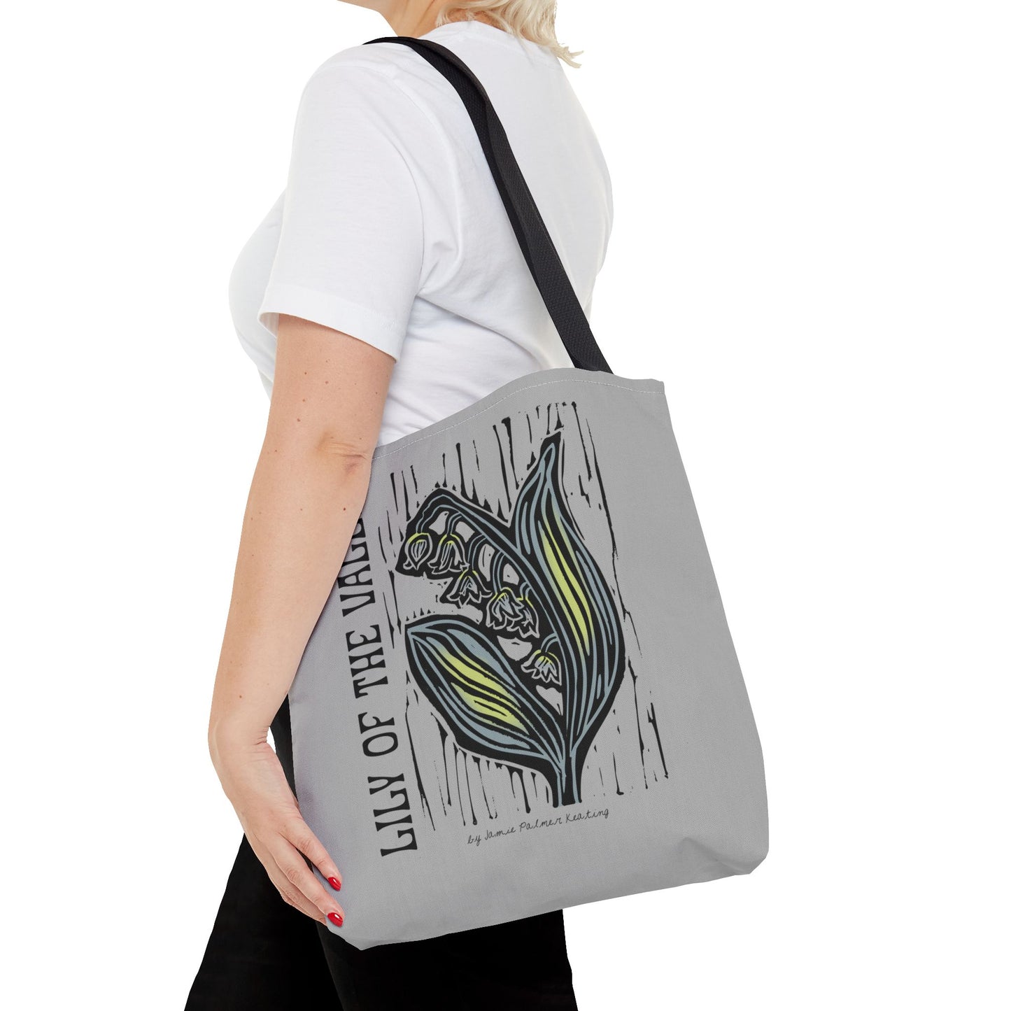 Person holding a tote bag with 'Lily of the Valley' design on a gray background