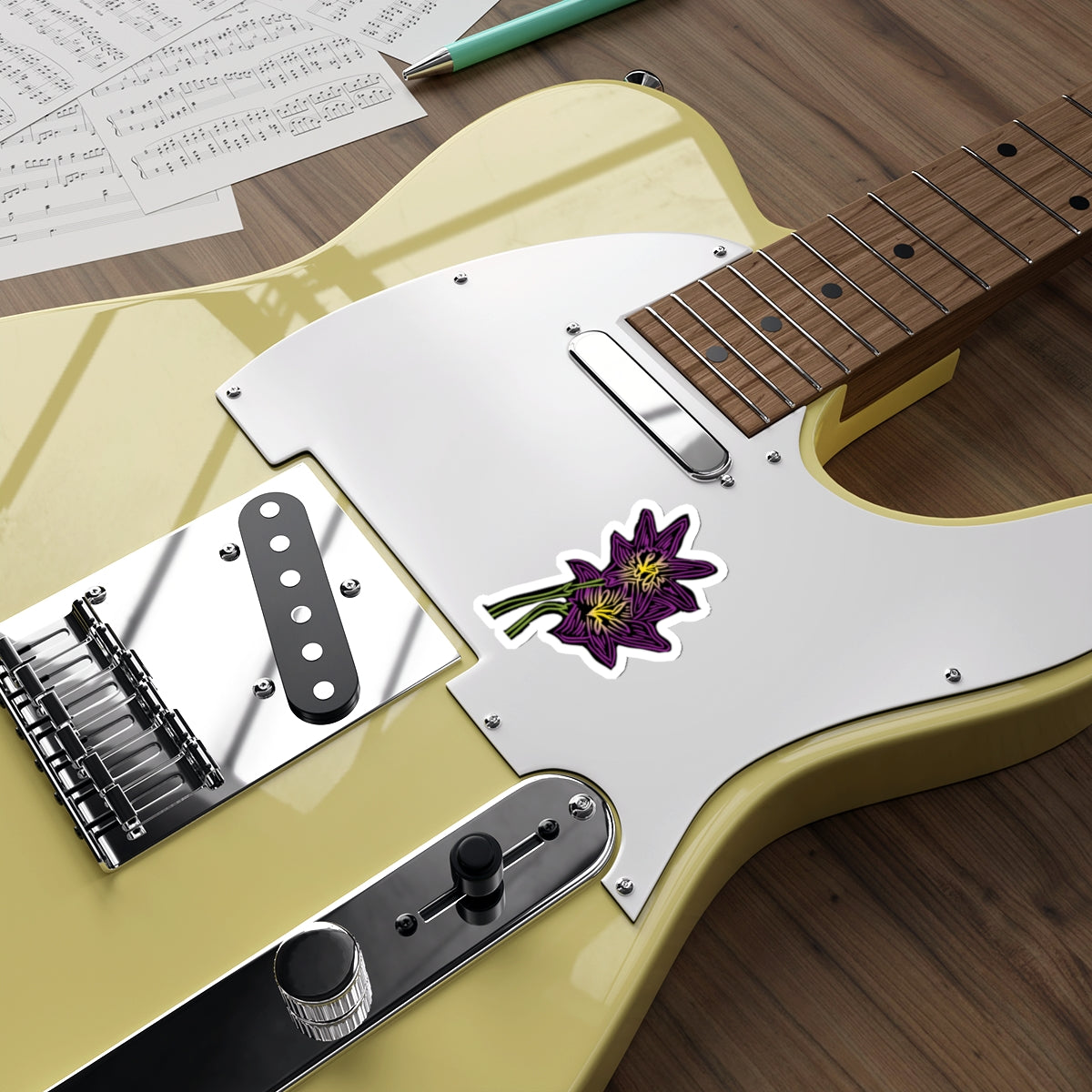 Close-up of a guitar with a sticker on the body, placed on a wooden surface with music sheets and a pen.