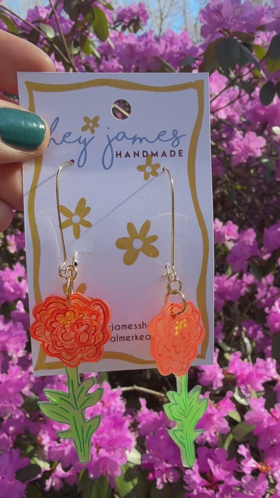 Hand holding a card with floral earrings against a background of pink flowers video