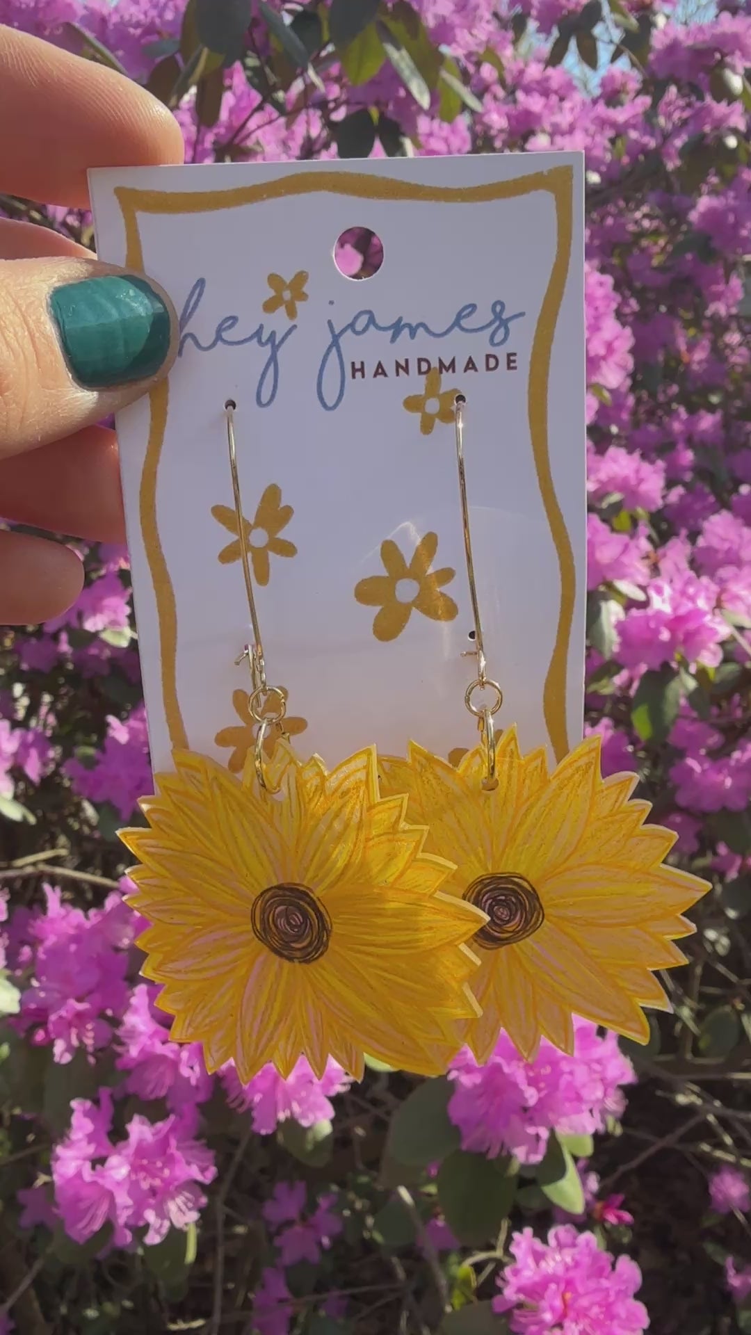 Yellow sunflower earrings on a card with a blurred background of pink flowers