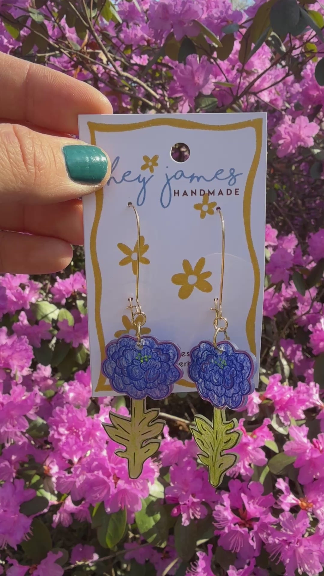 Hand holding a card with floral earrings against a background of pink flowers video