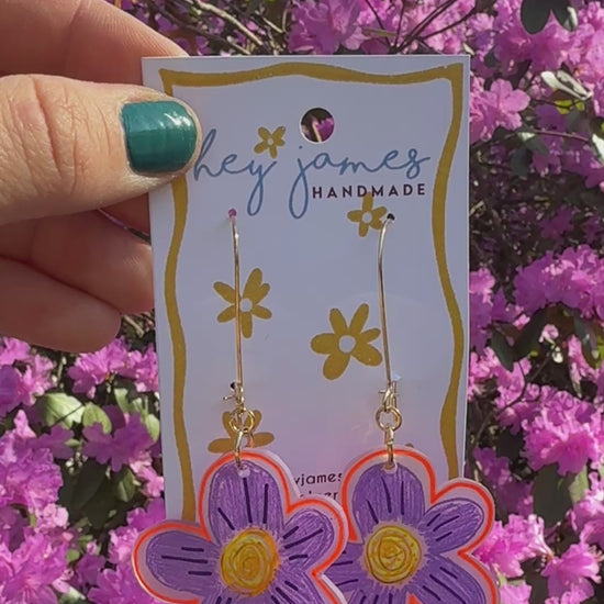 Flower-shaped earrings on a 'hey james handmade' card with pink flowers in the background video