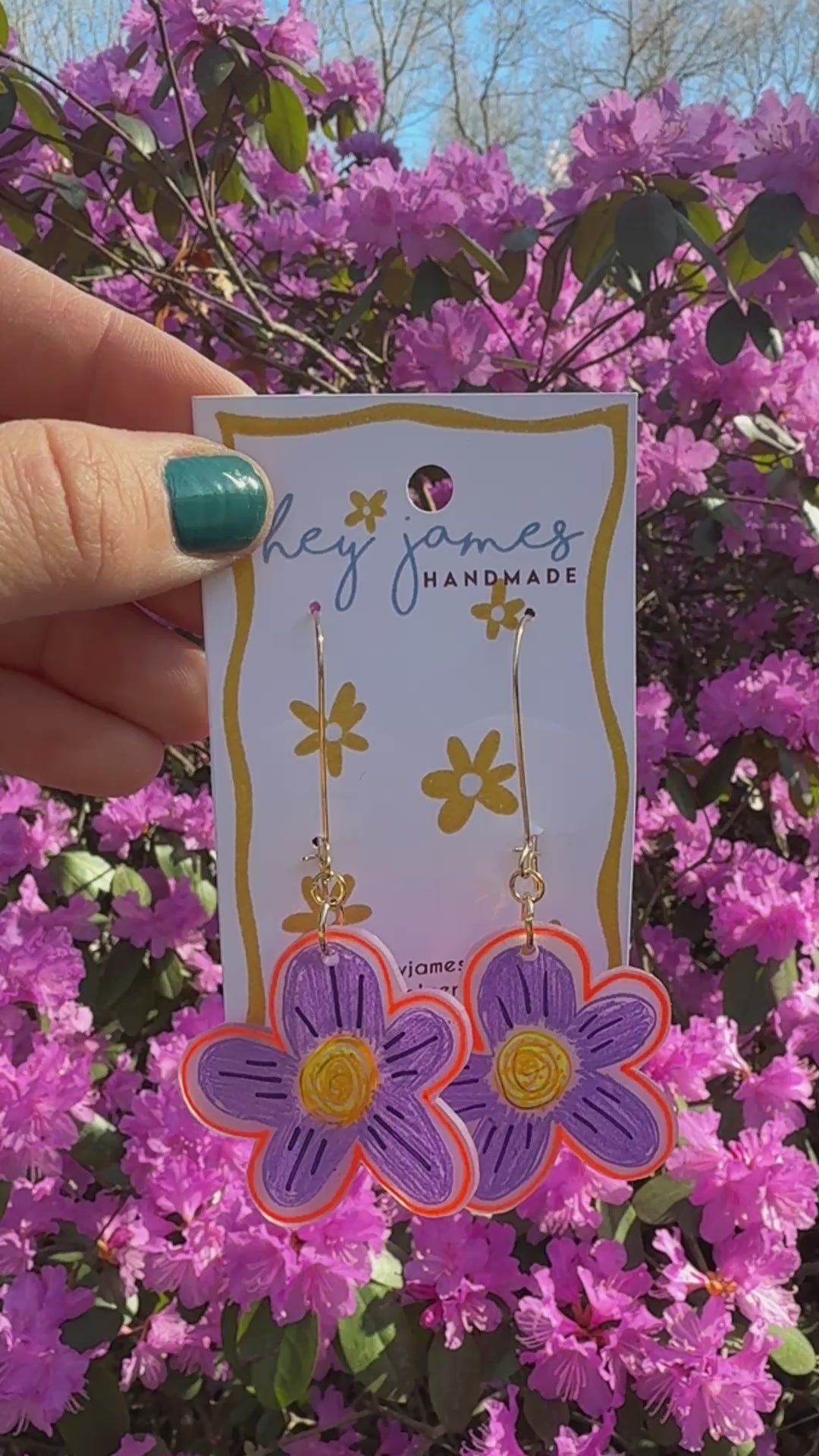 Flower-shaped earrings on a 'hey james handmade' card with pink flowers in the background video