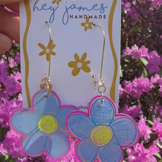 Flower-shaped earrings on a 'hey james handmade' card with pink flowers in the background video
