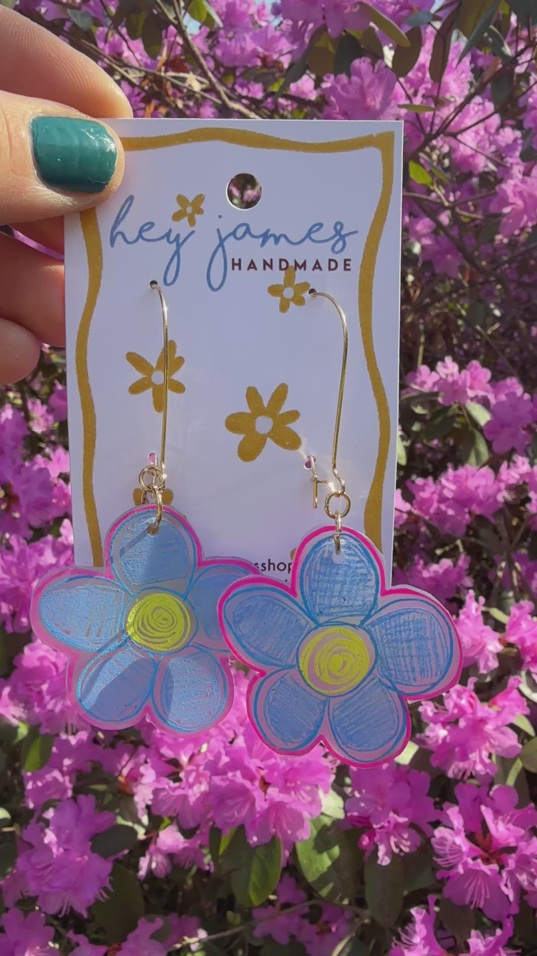 Flower-shaped earrings on a 'hey james handmade' card with pink flowers in the background video