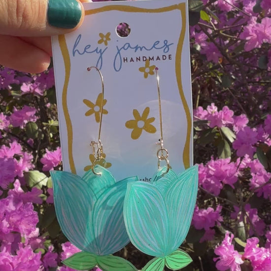 Blue earrings hanging on a card in front of pink flowers