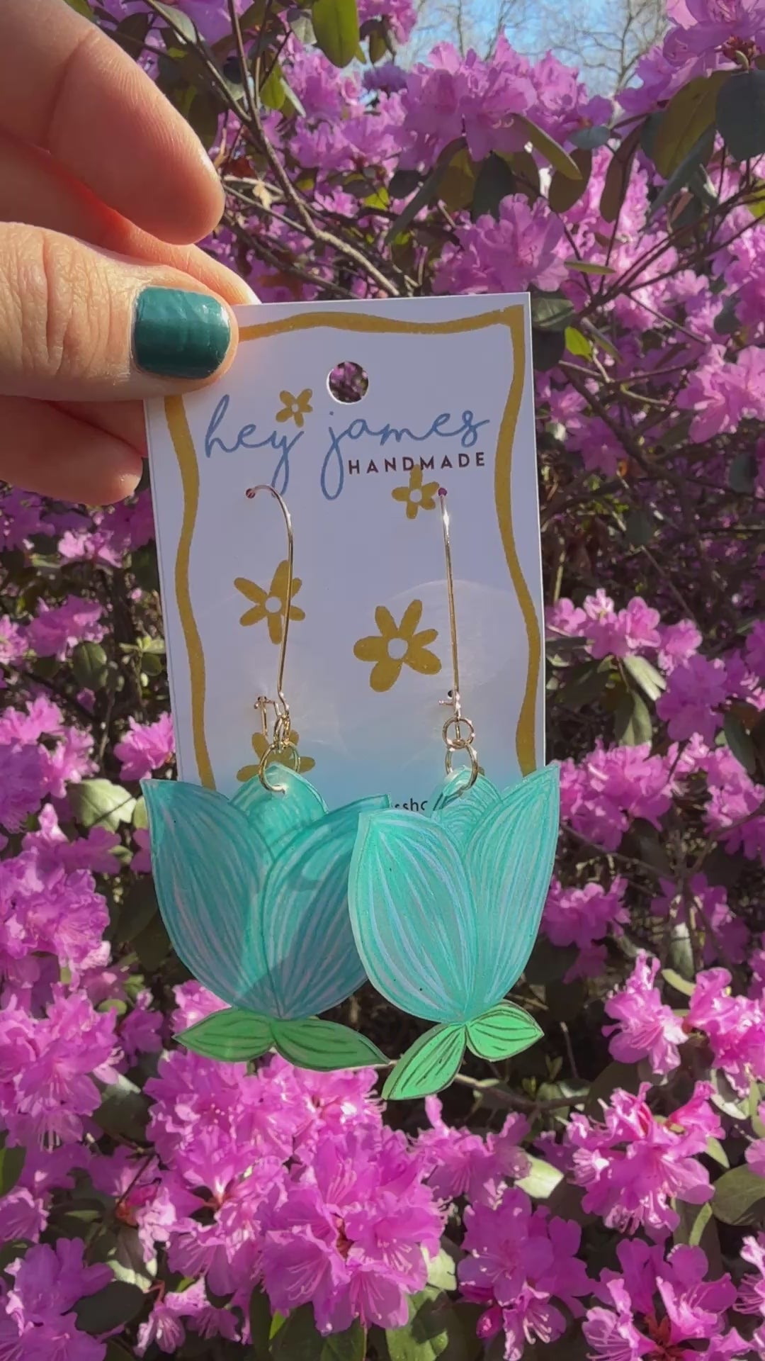 Blue earrings hanging on a card in front of pink flowers