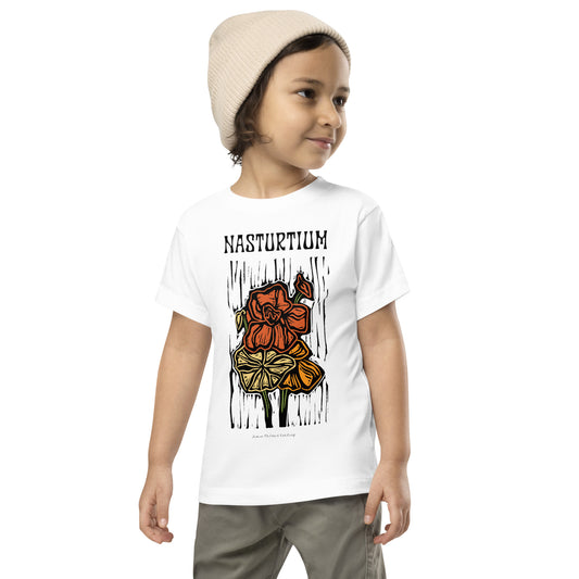 A child wearing a white short-sleeve graphic T-shirt with the word 'NASTURIUM' and a stylized flower illustration on the front, paired with gray pants and a beige knit beanie, against a plain white background.