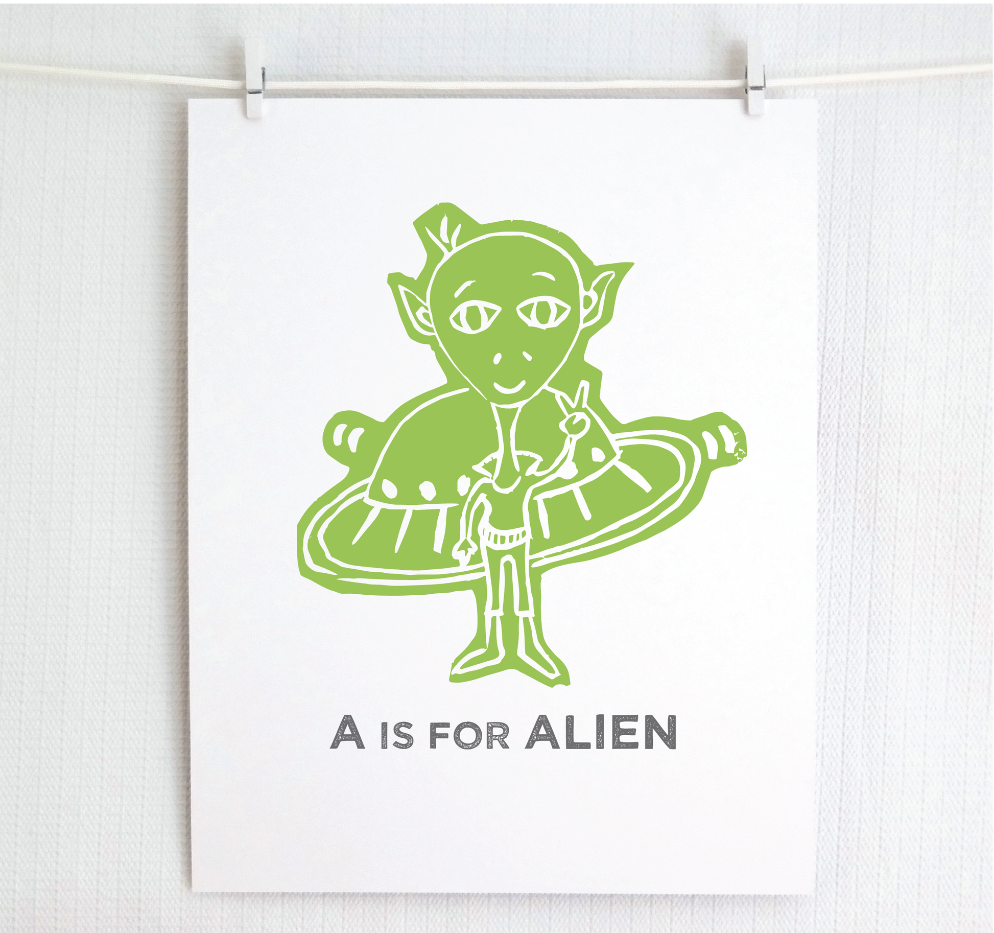 Friendly illustrated alien giving the peace sign in front of his UFO with "A is for Alien" text in a gray block font below. 
