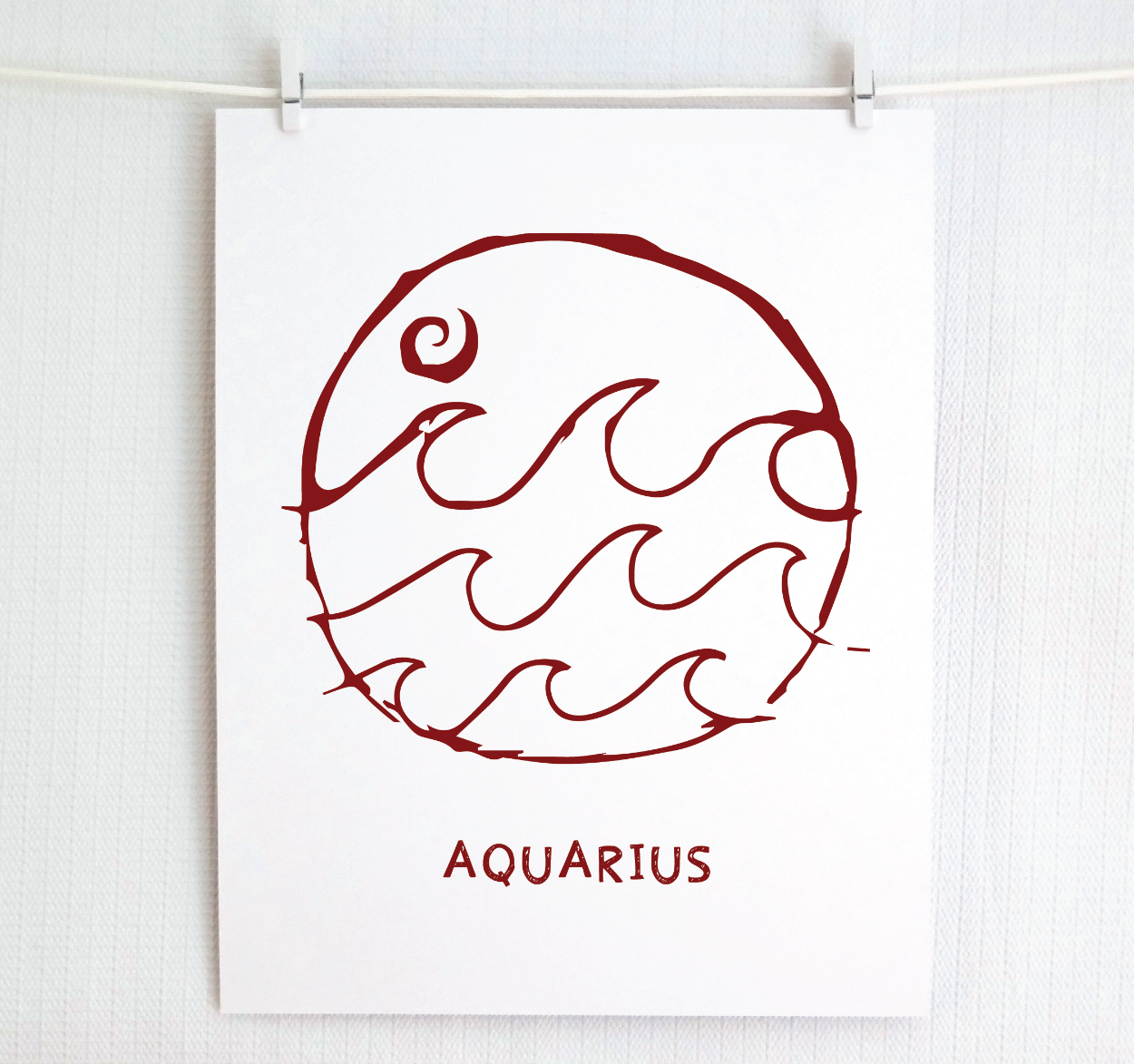 An illustration of the Aquarius Zodiac sign, printed on paper with the word 'AQUARIUS' at the bottom in cranberry