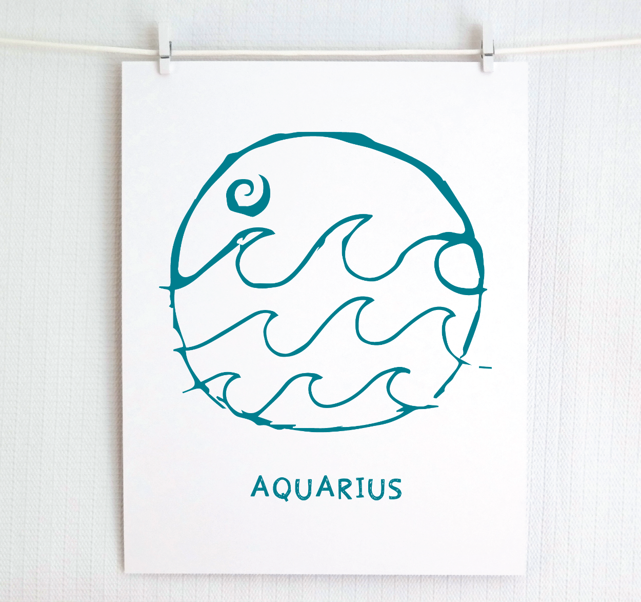 An illustration of the Aquarius Zodiac sign, printed on paper with the word 'AQUARIUS' at the bottom in dark teal