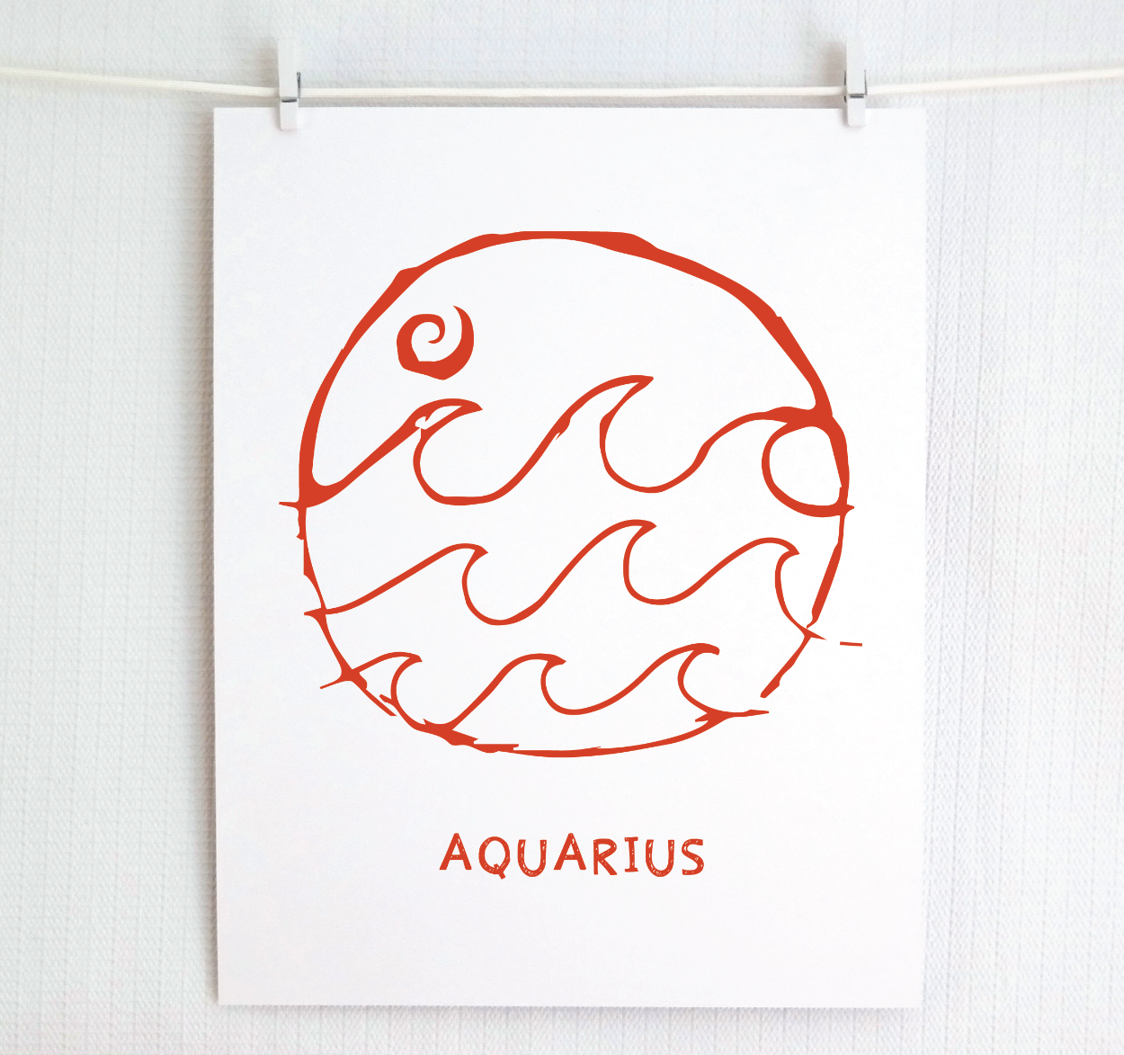 An illustration of the Aquarius Zodiac sign, printed on paper with the word 'AQUARIUS' at the bottom in red