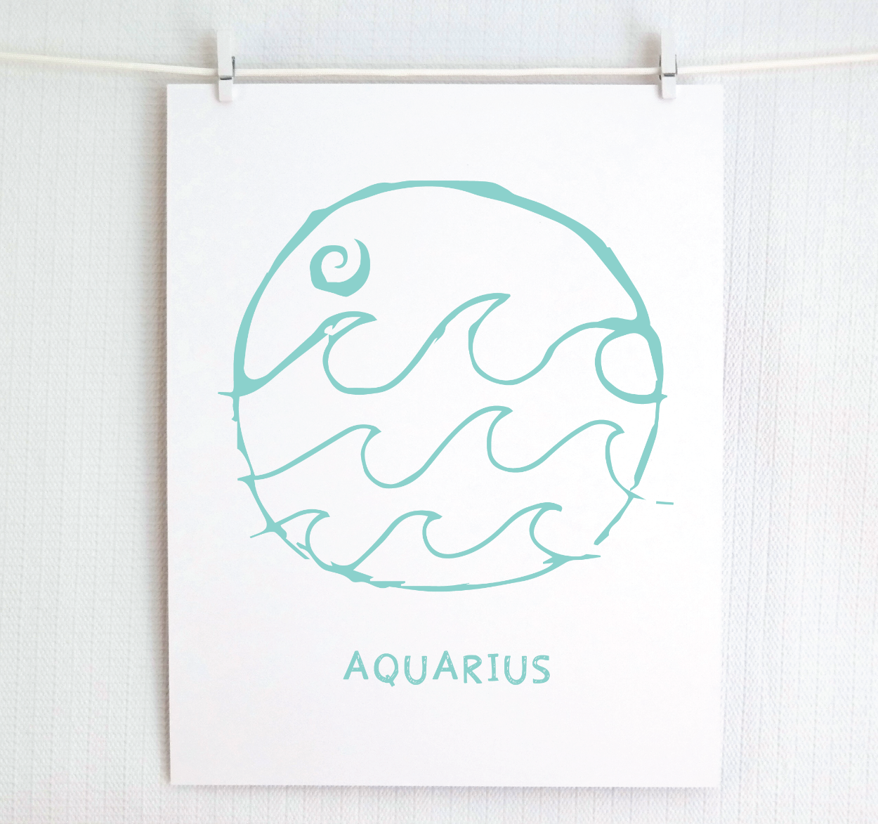 An illustration of the Aquarius Zodiac sign, printed on paper with the word 'AQUARIUS' at the bottom in light teal