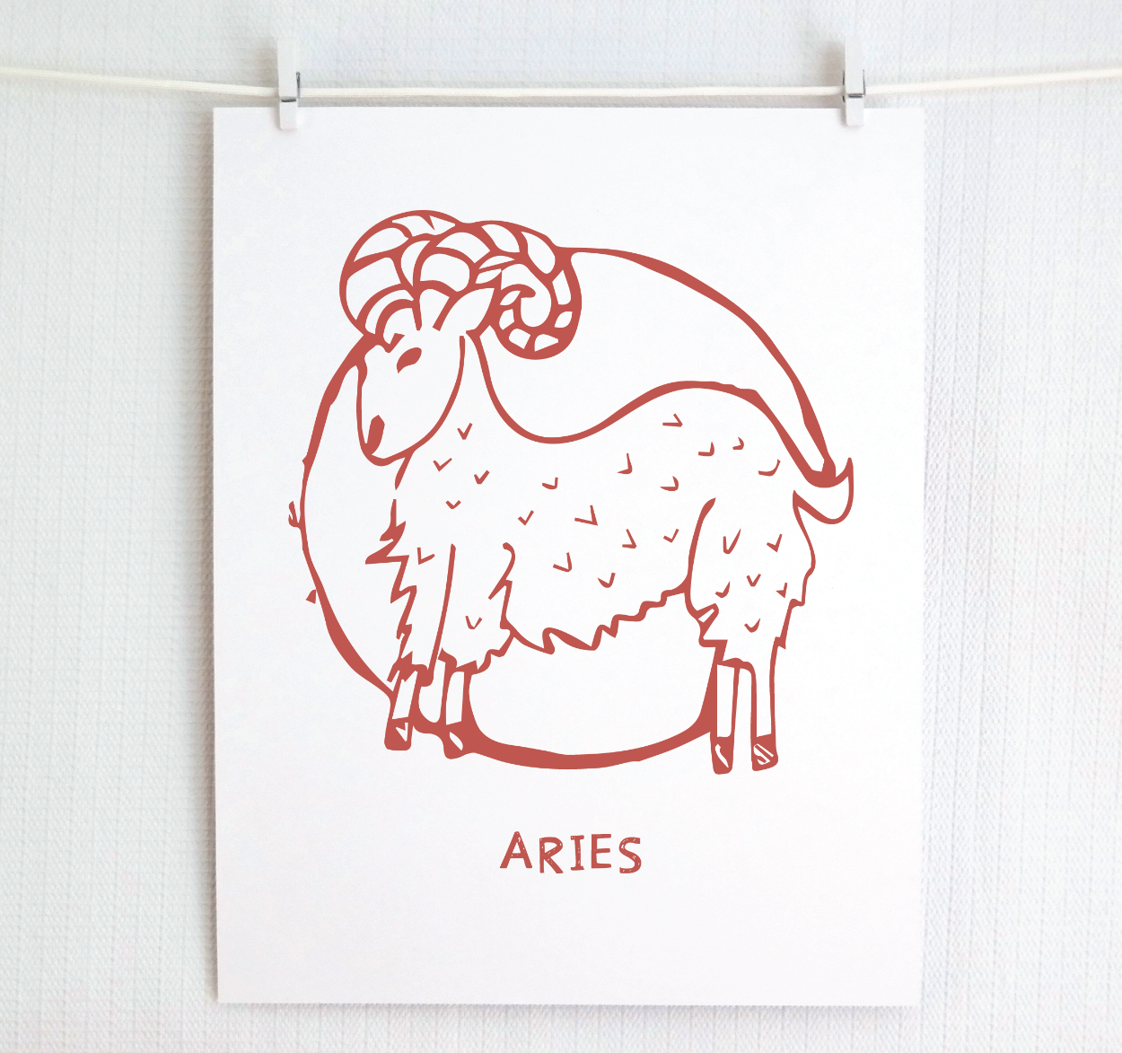 An illustration of the ARIES Zodiac sign as a ram, printed on paper with the word ‘ARIES’ at the bottom in blush.